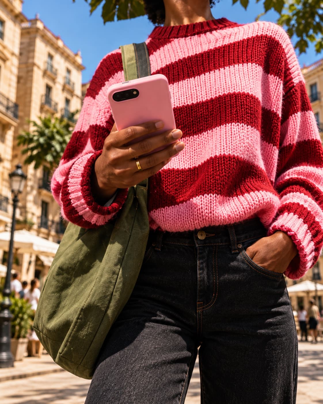 A person in a striped jumper holding their phone in the street.